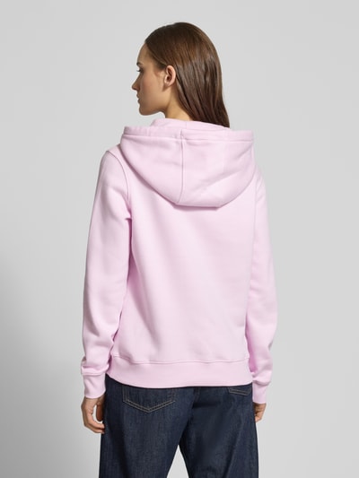 Vrouwenmodel draagt Regular Fit Sweatjacke aus Baumwoll-Mix van Tommy Jeans in lichtroze, katoenmix, capuchon, kangoeroezak, lange mouw, ribboorden, geheel effen, rugaanzicht.