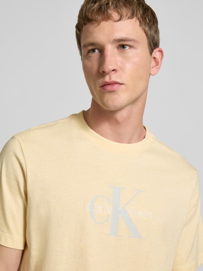 Männermodel trägt T-Shirt mit Label-Print und Rundhalsausschnitt von Calvin Klein Jeans in Gelb, Reine Baumwolle, Regular-Fit, Nahaufnahme Oberkörper.