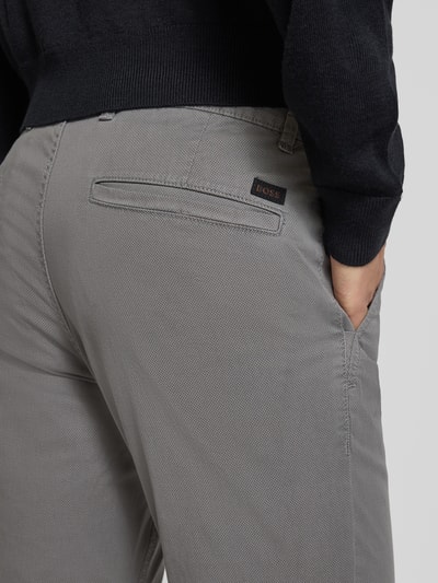Męski model nosi Slim Fit Chino aus Baumwoll-Mix Model 'CHINO_SLIM' od BOSS, fakturowany wzór na całej powierzchni, naszywka z logo, szlufki na pasek, kieszenie z boku i z tyłu, kolor szary, mieszanka bawełny. Zbliżenie tylnej części.