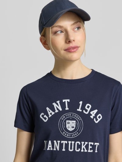 Frauenmodel trägt T-Shirt mit Label-Print von GANT in Dunkelblau aus reiner Baumwolle, Regular-Fit, Rundhalsausschnitt, Nahaufnahme Oberkörper.