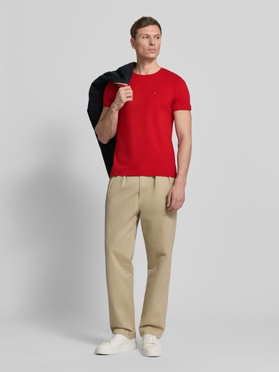 Männermodel trägt Slim Fit T-Shirt aus Baumwoll-Mix von Tommy Hilfiger in Rot mit Logo-Detail, unifarben, Kurzarm, Ganzkörperansicht von vorne.