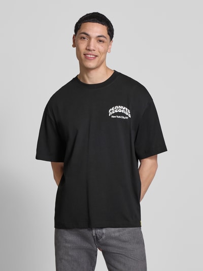 Männermodel trägt Regular Fit T-Shirt aus reiner Baumwolle Modell 'PEANUTS' von Only & Sons in Schwarz mit Peanuts® Print, Ganzkörperansicht von vorne.