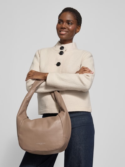 Frauenmodel trägt Hobo Bag mit Label-Detail Modell 'FARRAH' von LIEBESKIND BERLIN in Beige mit Tragehenkel und Label, Nahaufnahme Oberkörper.