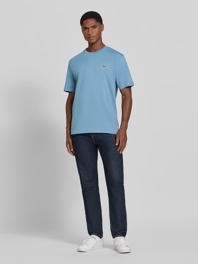 Männermodel trägt Regular Fit T-Shirt aus reiner Baumwolle von Lacoste in Hellblau und Jeans, Ganzkörperansicht von vorne. Herren T-Shirt von Lacoste