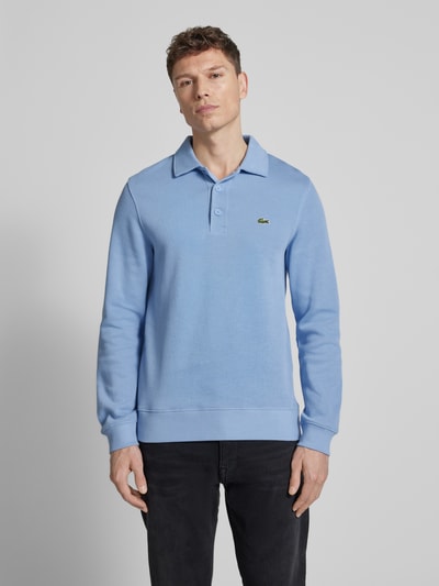 Männermodel trägt Regular Fit Sweatshirt aus reiner Baumwolle von Lacoste in Hellblau, Langarm, Polokragen, Logo-Stitching, Ganzkörperansicht von vorne.