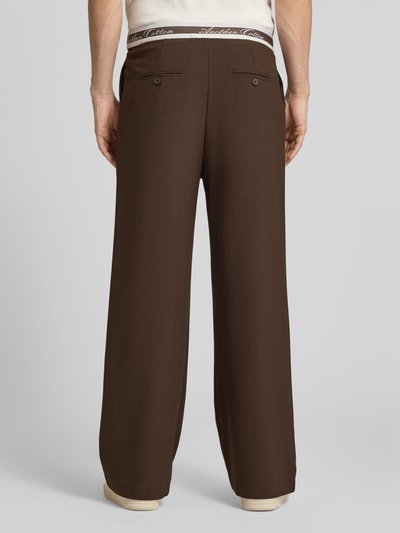 Männermodel trägt Stoffhose mit Logo-Bund und Gesäßtaschen von ANOTHER COTTON LAB aus Material-Mix mit Stretch-Anteil, Wide-Fit, braun, Ganzkörperansicht Rückansicht.