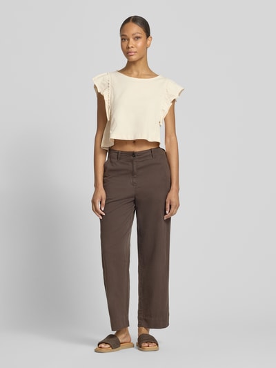 Frauenmodel trägt T-Shirt mit Schmetterlingsärmeln Modell 'MIRIEL' von Drykorn aus reiner Baumwolle, Loose Fit, U-Boot-Ausschnitt, helle Farbe mit Häkelspitze, kombiniert mit dunkler Hose, Ganzkörperansicht von vorne.