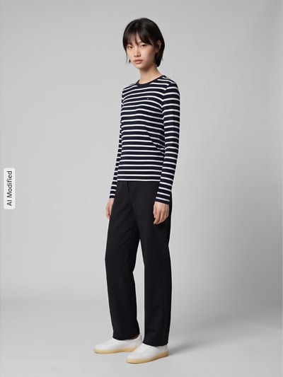 Frauenmodel trägt Slim Fit Langarmshirt aus reiner Baumwolle von Tommy Hilfiger, schwarz-weiß gestreift, kombiniert mit dunkler Hose, Ganzkörperansicht von vorne, Damen Langarmshirt von Tommy Hilfiger, KI-modifiziertes Bild.