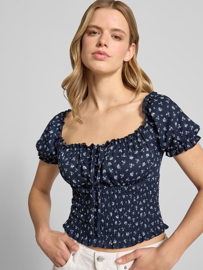 Frauenmodel trägt Slim Fit Blusentop mit Allover-Muster Modell 'HILLARY' von Only in Cropped-Länge, floral, Henley-Ausschnitt, kurzarm, Raffungen, dunkles Blau mit weißen Blüten, strukturierte Oberfläche, Nahaufnahme Oberkörper.