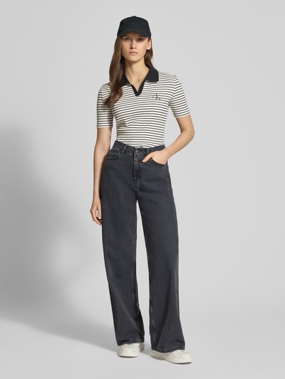 Frauenmodel trägt Slim Fit Poloshirt mit Label-Stitching von Calvin Klein Jeans im Baumwoll-Elasthan-Mix, Ripp-Optik, V-Ausschnitt, gestreift, Ganzkörperansicht von vorne.