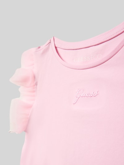 Mädchen trägt T-Shirt mit Logo-Stitching und Rundhalsausschnitt von Guess in Rosa, Tüll am Ärmel, Nahaufnahme Oberkörper.