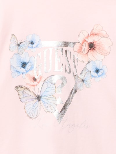 Mädchen trägt Longsleeve mit Label-Print von Guess in zartrosa mit Blumen und Schmetterlingen, Baumwoll-Elasthan-Mix, Nahaufnahme Oberkörper.