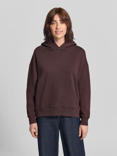 Frauenmodel trägt Oversized Hoodie aus Baumwolle von Closed in Dunkelbraun mit überschnittenen Schultern und Print, glatte Textur, Ganzkörperansicht von vorne.