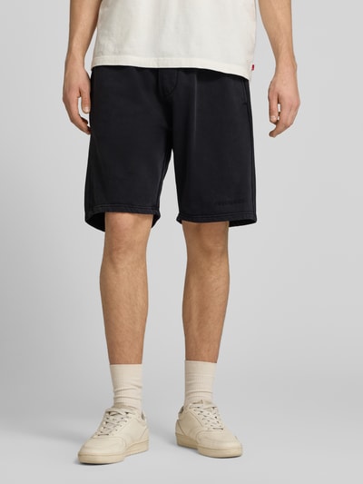 Männermodel trägt Shorts mit elastischem Bund und Logo-Stitching von Pegador aus Baumwoll-Mix, Loose-Fit, schwarz, Nahaufnahme Unterkörper.