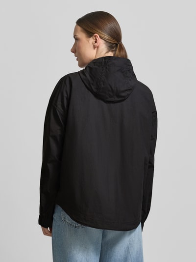 Frauenmodel trägt Jacke mit Kapuze und Zweiwege-Reißverschluss von camel active, prosty krój, regulowane zakończenia rękawów, długość tyłu w rozmiarze 36: 67 cm, szerokość ramion w rozmiarze 36: 44 cm, szerokość klatki piersiowej w rozmiarze 36: 63 cm, długość rękawów w rozmiarze 36: 62 cm, czarna kolorystyka, tekstura gładka, wpuszczane kieszenie, całkowity widok z tyłu