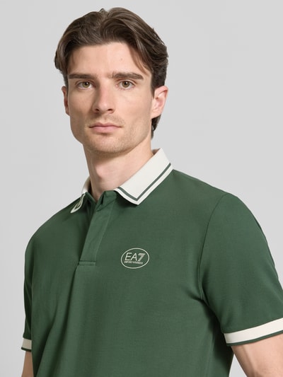 Mężczyznamodel nosi Regular Fit Poloshirt mit Logo-Print von EA7 Emporio Armani, zielony, krój regular fit, bawełna elastyczna, logo, kołnierzyk polo, krótki rękaw, długość tyłu w rozmiarze M: 68 cm, zbliżenie na górną część ciała