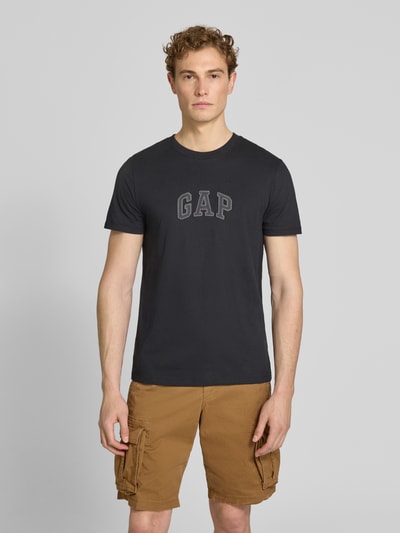 Männermodel trägt T-Shirt mit Logo-Patch und Rundhalsausschnitt von GAP aus reiner Baumwolle, Straight Fit, schwarze Farbe, Ganzkörperansicht von vorne. Rückenlänge bei Größe M: 70 cm.