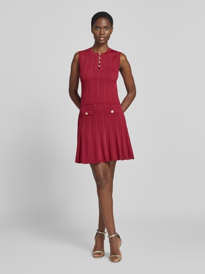 Frauenmodel trägt Stricktop in Pointelle-Strick mit kurzer Knopfleiste von GUESS, körpernaher Schnitt, Viskose-Mix in Rot, Ganzkörperansicht von vorne.