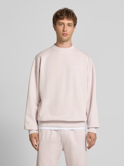 Männermodel trägt Oversized Sweatshirt mit Label-Stitching von Pegador in Hellrosa aus Baumwoll-Mix, Rundhalsausschnitt, Ganzkörperansicht von vorne.