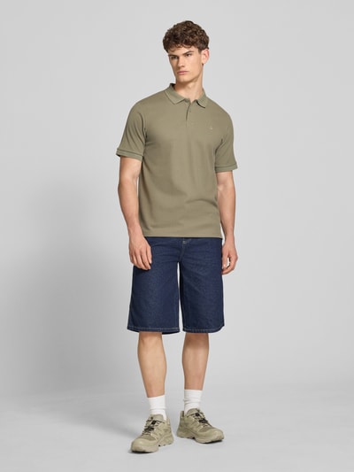Männermodel trägt Regular Fit Poloshirt mit Strukturmuster Modell 'AUSTIN' von Jack & Jones in Oliv, kurze Knopfleiste, Ganzkörperansicht von vorne.
