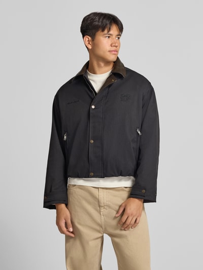 Männermodel trägt schwarze Twill Jacke mit Label- und Motiv-Stitching von ANOTHER COTTON LAB, strukturierte Oberfläche, Ganzkörperansicht von vorne.