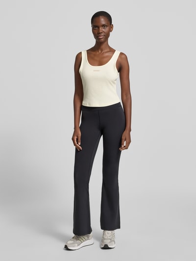 Modelka nosi Slim Fit Top mit Logo-Stitching Modell 'Circe' od Guess Activewear, kremowy, elastyczna bawełna, krój slim fit, widok całej sylwetki z przodu.