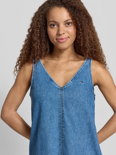 Frauenmodel trägt Ausgestelltes Jeanskleid aus reiner Baumwolle von Tommy Jeans in Denim-Optik mit V-Ausschnitt, Label-Patch, Label-Stitching, Nahtreißverschluss, schmale Träger, ohne Ärmel, Mini-Länge, seitliche Eingrifftaschen, Twill-Materialverarbeitung, reine Baumwolle, Nahaufnahme Oberkörper.
