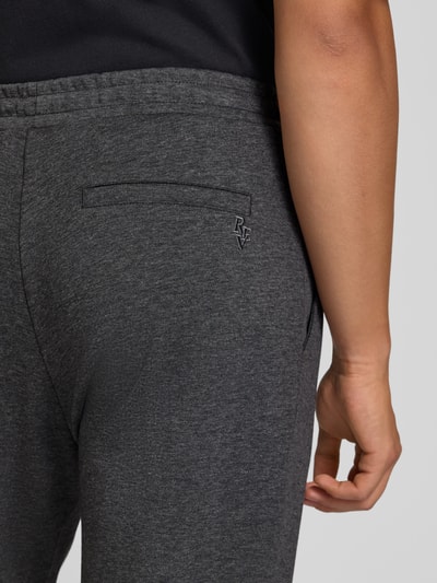Mężczyzna nosi spodnie dresowe Straight Fit Sweatpants mit elastischem Bund od REVIEW, Mieszanka materiałów z mieszanką bawełny, kanty, elastyczny pas, Szerokość w rozmiarze M: 42 cm, Długość wewnętrzna nogawki w rozmiarze M: 82 cm, ciemnoszary kolor, melanżowa tekstura, detal tylnej kieszeni, detalaufnahme.