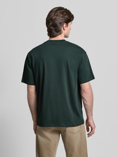 Männermodel trägt Regular Fit T-Shirt aus reiner Baumwolle Modell 'Baine' von WOODBIRD in Dunkelgrün, glatte Textur, Ganzkörperansicht Rückansicht.