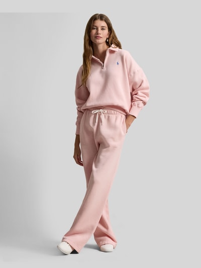 Frauenmodel trägt Sweatshirt mit Label-Stitching von Polo Ralph Lauren in Rosa mit Polokragen, kurzem Reißverschluss, lockerer Schnitt, Baumwoll-Mix, gerippte Abschlüsse, Ganzkörperansicht von vorne.