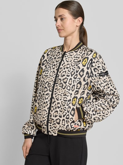 Frauenmodel trägt Blouson mit Eingrifftaschen Modell 'SUZY BLUE' von Frieda & Freddies im Material-Mix mit Stretch-Anteil, Loose-Fit, Allover-Leo-Muster in Beige, Schwarz und Gelb, elastische Abschlüsse, Reißverschluss, Label-Detail, Nahaufnahme Oberkörper.