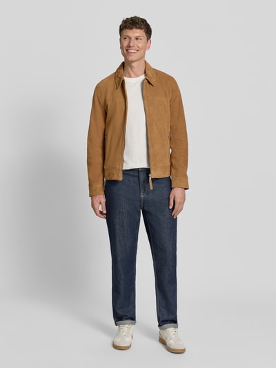 Mannenmodel draagt Lederjacke aus Schafsnubuk met Reißverschluss Modell 'TRIVEN' van MAURITIUS, regular fit, platte kraag, ritszakken, camelbruin, jeans, witte sneakers. Ganzkörperansicht van voren.