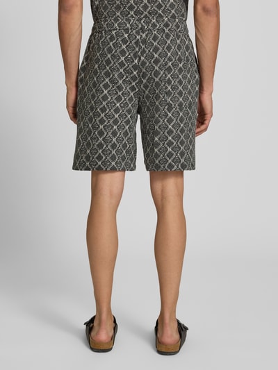 Männermodel trägt Shorts im Allover-Look mit Kordelzug Modell 'CARLOS' von Redefined Rebel aus Reine Baumwolle, Ganzkörperansicht Rückansicht. Regular-Fit, elastischer Bund, dunkles Muster, Bundweite bei Größe M: 40 cm, Innenbeinlänge: 19 cm.