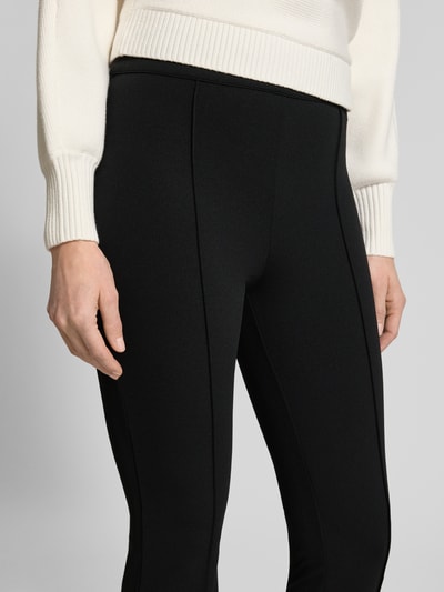 Frauenmodel trägt Flared Fit Stoffhose mit elastischem Bund Modell 'Evelina' von Guess in Schwarz, elastischer Material-Mix, Nahaufnahme Oberkörper.