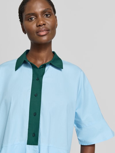 Frauenmodel trägt Relaxed Fit Kurzarmbluse aus reiner Baumwolle Modell 'KAYLEE' von Essentiel Antwerp in Hellblau und Dunkelgrün, Nahaufnahme Oberkörper. Damen Kurzarmbluse von Essentiel Antwerp.