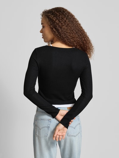 Frauenmodel trägt Slim Fit Longsleeve mit Strukturmuster von Guess Jeans in Schwarz, Elastischer-Material-Mix, Layered-Look, Rückenlänge 47 cm, Ganzkörperansicht Rückansicht.