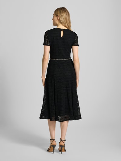 Frauenmodel trägt Midikleid mit Gürtel in Gliederketten-Optik von MICHAEL Michael Kors in Schwarz, Material-Mix mit Stretch-Anteil, taillierter Schnitt, Rundhalsausschnitt, blickdichtes Unterkleid, Schlüsselloch-Ausschnitt, Ganzkörperansicht Rückansicht.