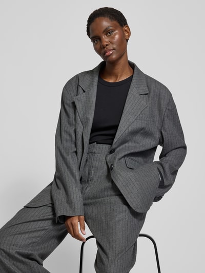 Frauenmodel trägt Relaxed Fit Blazer aus Viskose-Mix von black palms mit Logo-Patch und Paspeltaschen in Grau, Nahaufnahme Oberkörper.