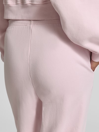 Frauenmodel trägt Sweatpants aus reiner Baumwolle mit Logo-Print Modell 'PLIZZY' von American Vintage in Hellrosa, glatte Textur, elastischer Bund, Eingrifftaschen, Straight Fit, Detailaufnahme Nahaufnahme Oberschenkel und Hüfte, Damen Sweatpants.