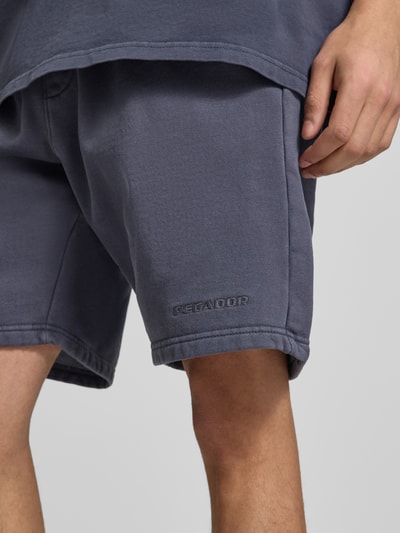 Männermodel trägt Shorts mit elastischem Bund und Logo-Stitching von Pegador aus Baumwoll-Mix im Loose-Fit, Nahaufnahme Oberschenkel.