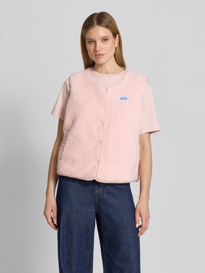 Frauenmodel trägt Regular Fit Weste in Teddy-Optik Modell 'AMALIA' von VILLA SOPHIE in hellrosa, mit Druckknopfleiste, Label-Patch, seitlichen Eingrifftaschen, Materialverarbeitung Teddyfell, Ganzkörperansicht von vorne.