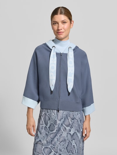 Frauenmodel trägt Relaxed Fit Sweatjacke aus Viskose-Mix mit Logo-Detail von Marc Cain, Kapuze, Reißverschluss, elastischer Bund, Ganzkörperansicht von vorne.
