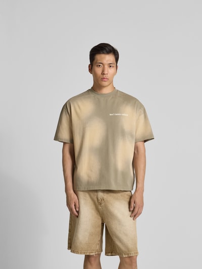 Männermodel trägt T-Shirt mit Label-Print von Don’t Waste Culture in Beige mit Rundhalsausschnitt und geradem Schnitt, Nahaufnahme Oberkörper.