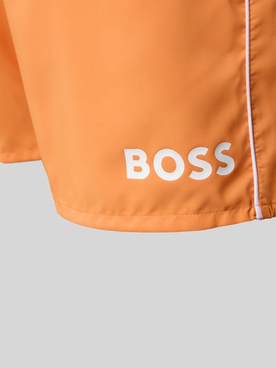 Männermodel trägt Badehose mit Paspelnaht in Kontrastfarbe Modell STARFISH von BOSS, unifarben, Label-Schriftzug, Nahaufnahme Oberschenkel.