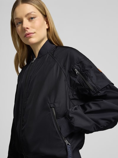Frauenmodel trägt Bomberjacke mit Reißverschlusstaschen Modell 'LIL' von SAVE THE DUCK in Schwarz, Material-Mix mit Stretch-Anteil, Nahaufnahme Oberkörper. Rückenlänge bei Größe S: 53 cm, Schulterbreite 42 cm, Brustweite 61 cm, Ärmellänge 70 cm, Regular-Fit, Stehkragen, Reißverschluss.