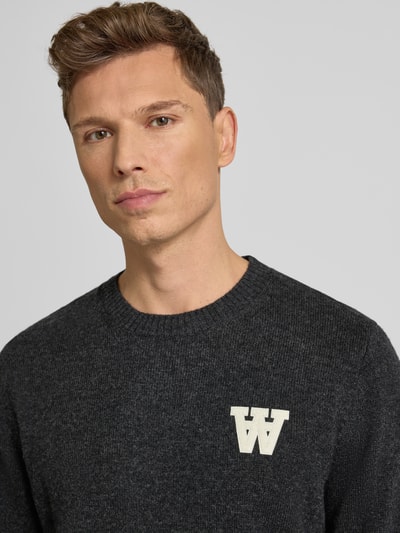 Männermodel trägt Strickpullover aus Lammwolle Modell 'Tay' von Wood Wood, Regular-Fit, Rundhalsausschnitt, Label-Stitching, Nahaufnahme Oberkörper.