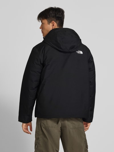 Männermodel trägt Jacke mit Logo und Ärmelriegeln von The North Face in Schwarz, Kapuze, Regular Fit, Ganzkörperansicht Rückansicht. Rückenlänge etwa 70 cm, Schulterbreite ca. 49 cm, Brustweite ca. 60 cm, Ärmellänge ca. 67 cm.