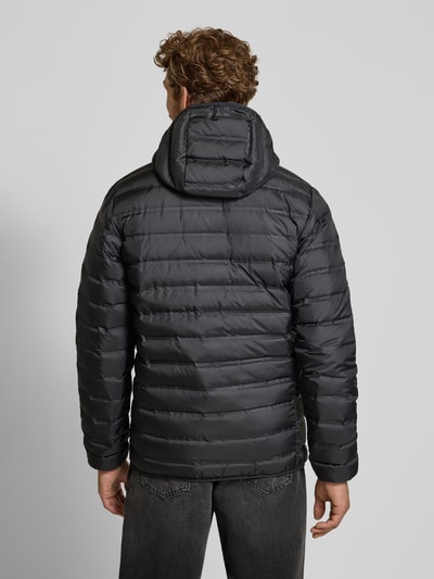 Männermodel trägt czarną kurtkę pikowaną o kroju regular fit z kapturem, nadrukiem z logo, zamek błyskawiczny, Model 'Lake 22™' od Columbia, Długość tyłu w rozmiarze M: 72 cm, szerokość ramion w rozmiarze M: 43 cm, szerokość klatki piersiowej w rozmiarze M: 42 cm, długość rękawów w rozmiarze M: 70 cm, z efektem pikowania, widok całej sylwetki od tyłu.