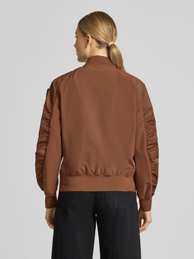 Frauenmodel trägt Bomberjacke mit Reißverschlusstaschen Modell 'LAURIE' von Blauer Usa in Braun, Loose-Fit, Stehkragen, Rückenlänge 57 cm, Schulterbreite 44 cm, Brustweite 43 cm, Ärmellänge 62 cm, Label-Patches, Gerippte-Abschlüsse, Ganzkörperansicht Rückansicht.
