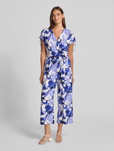 Modelka kobieca ma na sobie Relaxed Fit Jumpsuit mit V-Ausschnitt od Betty Barclay, elastyczna mieszanka materiałów, taliowany krój, dekolt w serek, krótki rękaw, kwiatowy nadruk na całej powierzchni, wpuszczane kieszenie, długość tyłu w rozmiarze 36: 43 cm, szerokość w rozmiarze 36: 49 cm, długość rękawów w rozmiarze 36: 22 cm, całkowita długość w rozmiarze 36: 132 cm, długość wewnętrzna nogawki w rozmiarze 36: 61 cm; kolory biały, niebieski, liliowy; faktura gładka, widoczny print, cała sylwetka z przodu